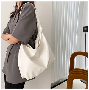 Close-up of a large white PU leather tote bag worn by a model in a minimalist room