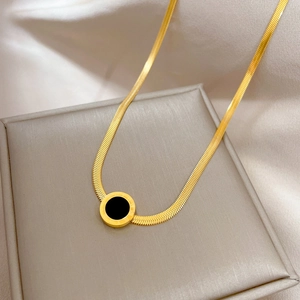 Gold Roman numeral necklace with round black pendant on beige textured jewelry box