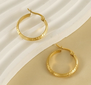 Detail of gold titanium steel hoop earrings with Greek key patterns and textured finish