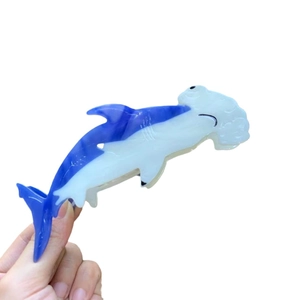 Blue and white shark-shaped acetate hair claw clip held against a white background
