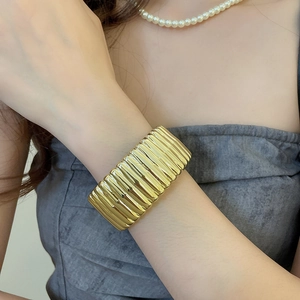 Close-up of golden wide metal elastic bracelet with textured ripple design on wrist