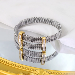 Detail view of a silver mesh bracelet with gold crystal clasps on a reflective surface