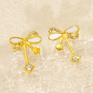 Detail of gold bow earrings with crystal star charms on a textured background