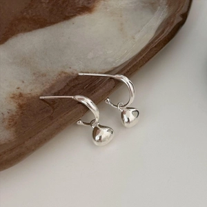 Close-up of elegant silver heart drop earrings on a textured ceramic dish plate