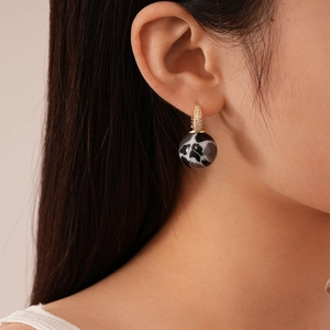 Detail of vintage geometric sphere earring with gold zircon clasp and marble texture