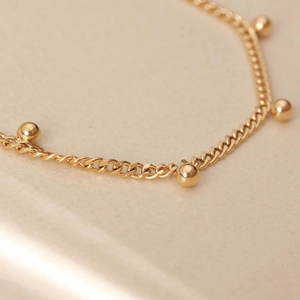 Macro detail of 18K gold plated curb chain with solid metal beads and polished finish