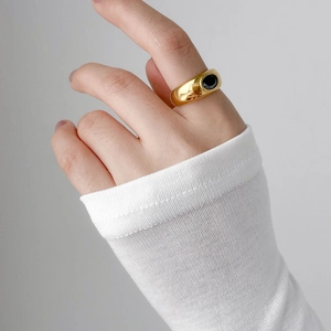 Close-up of a wide gold ring featuring a polished black oval gemstone on a hand
