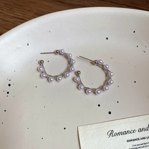 Detailed view of silver C-shaped pearl earrings on a vintage ceramic plate background