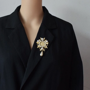 Baroque pearl brooch with coin design and leaf accents on a black blazer lapel