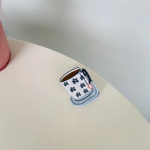 Detailed view of acrylic coffee cup hair claw clip with blue floral pattern on white base