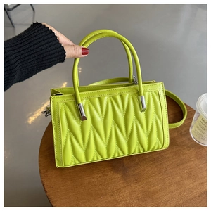 Detail of lime green V-quilted handbag with silver hardware and top handle on a table
