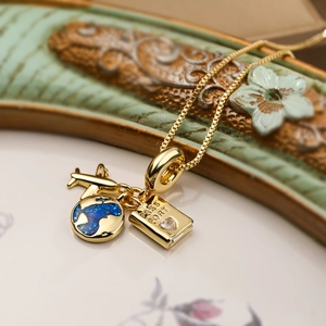 Close-up of gold travel necklace with airplane globe and passport charms on box chain
