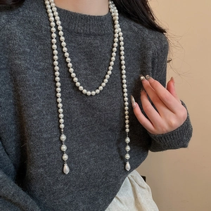 Detail of a vintage pearl necklace with long tassel and water-drop pendant on a grey sweater