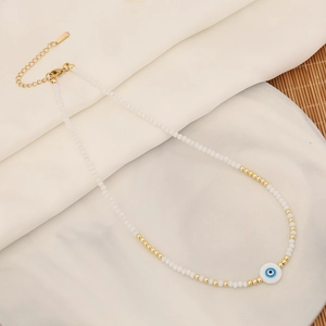 Detail of beaded evil eye necklace with gold spacers and blue heart shell charm on marble