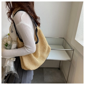 Hobo style woven straw bag with black leather strap worn over shoulder for summer style