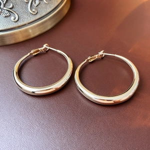 Polished gold round hoop earrings lying on a textured brown leather surface