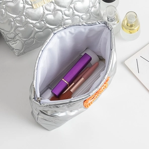 Détail d'une trousse à maquillage matelassée argentée montrant le rangement et le gland orange