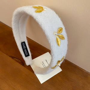 Detail of white plush headband featuring gold leaves, pearls, and handmade label