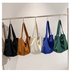 Detail of five colors of corduroy tote bags hanging on hooks against a neutral wall