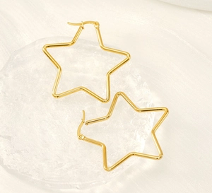 Macro detail of star-shaped gold-plated stainless steel earrings on a glass tray