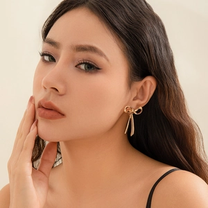 Detailed close-up of a gold bow-shaped earring with elegant snake chain tassels on a model
