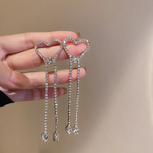 Détail de boucles d'oreilles cœur en strass avec de longs pompons sur un fond beige