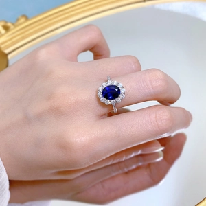 Macro shot of oval blue sapphire halo ring on finger with silver and diamond accents