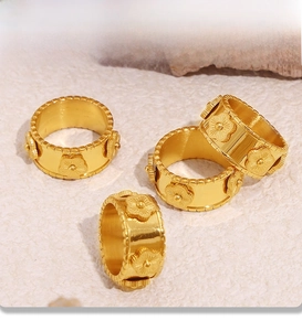 Dettaglio di anelli in acciaio inossidabile placcati oro 18k con rilievo floreale su sabbia