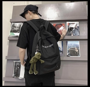 Détail d'un sac à dos en toile noire avec peluche de grenouille verte et texte blanc