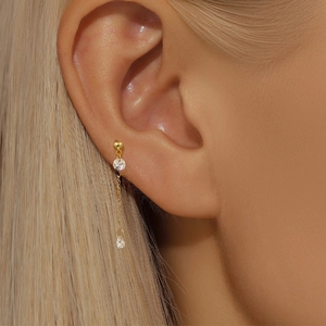Close-up of gold heart drop earring with zircon stones and tassel chain on model