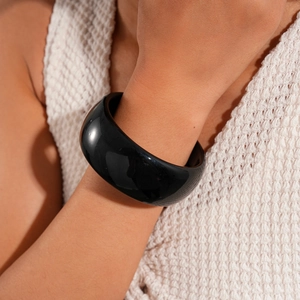 Close-up of a wide glossy black resin round bangle worn over a white knitted fabric sleeve