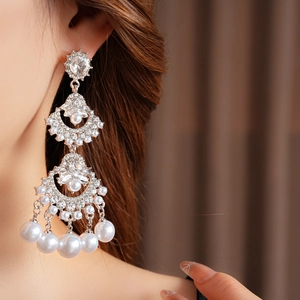 Detailed view of silver-tone tassel earrings with rhinestones and white pearls on a model