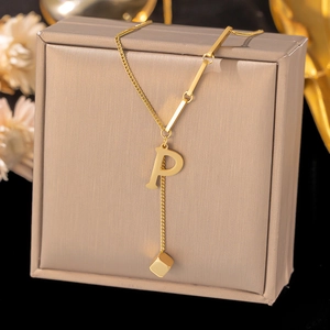 Detail of gold necklace featuring letter P pendant and geometric cube on a gift box