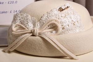 Detailed close-up of wool beret featuring delicate white lace trim and bow embellishment