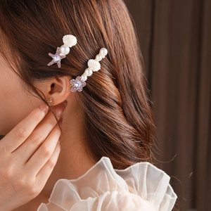 Détail de barrettes coquillages avec perles et strass sur cheveux bruns ondulés