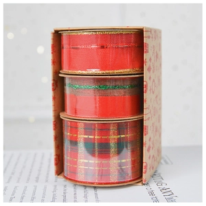 Close-up of three festive Christmas ribbon rolls in red and gold inside a kraft gift box