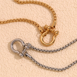 18K gold and silver horseshoe pendant necklaces with square link chains on beige background
