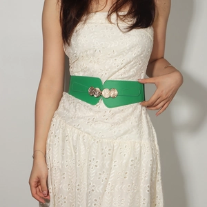 Detail of green elastic waist belt with gold interlocking buckle on white lace dress