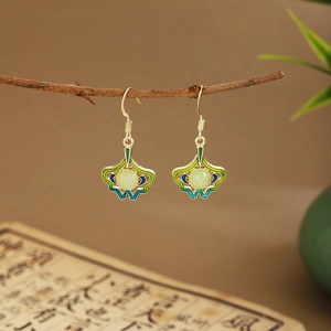 Detailed shot of green fan-shaped leaf earrings with tassels hanging on a branch
