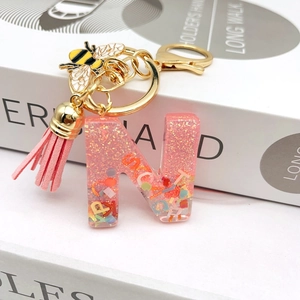 Macro detail of resin letter N keychain with pink glitter, bee charm, and suede tassel