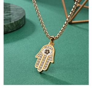 Detailed close-up of a gold Hamsa Hand pendant with zircon Evil Eye on a green base