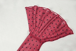 Close-up of red mesh fabric with black polka dots featuring fine overlock stitching detail
