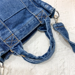 Detail of blue denim shoulder bag showing reinforced stitching and metal D-ring hardware