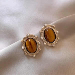 Macro detail of gold oval tiger eye earrings with pearl accents on silk background