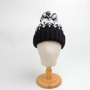 Close-up of thick winter knit beanie with geometric rhombus pattern and mixed pom-pom