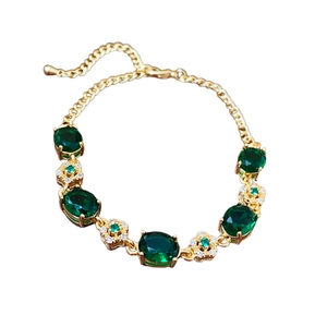 Gold plated bracelet with emerald flower charms and diamond accents on white background