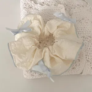 Close-up of cream-colored scrunchie with blue ribbon bows and delicate wavy edge detail