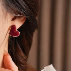 Detail of red velvet heart earring with gold border worn on a model's ear