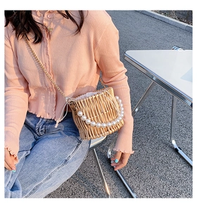 Detail of woven straw bucket bag with pearl handle and golden chain on a white table