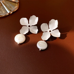 Detail of silver metallic flower earrings with white freshwater pearls on leather surface